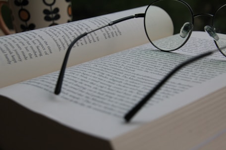 An open book with pages turning, surrounded by scattered notes and a pair of reading glasses.