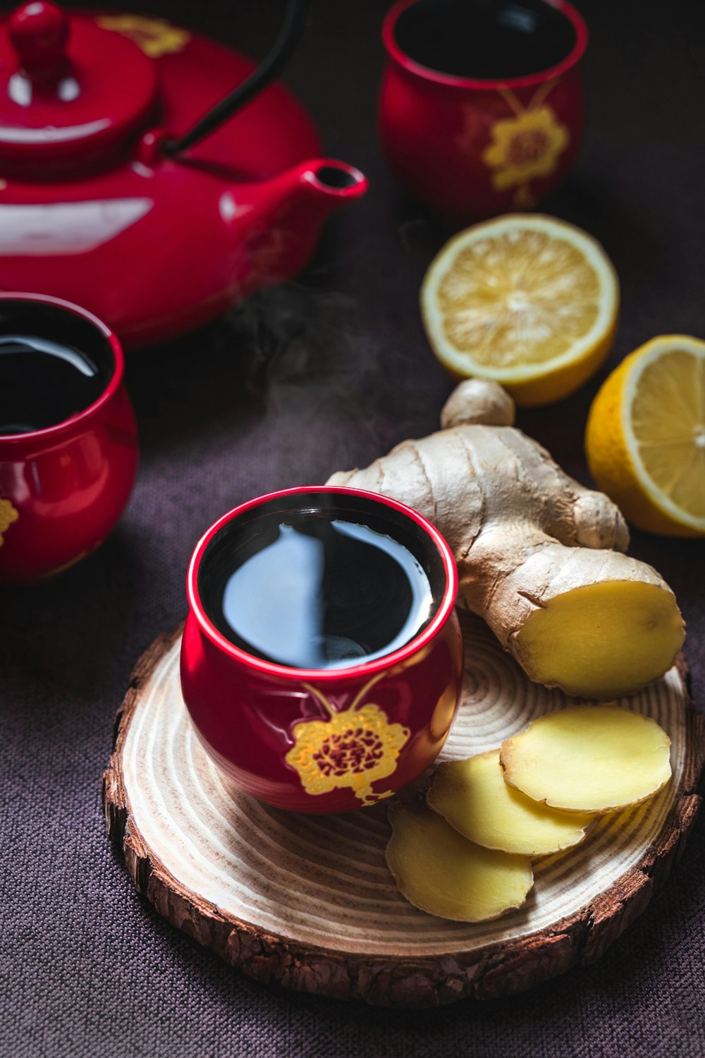 in Scheiben geschnittene Zitrone auf roter Keramikuntertasse neben rotem Keramikbecher mit schwarzer Flüssigkeit