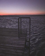 A rustic wooden dock stretching into calm tidal waters under a pastel sky.