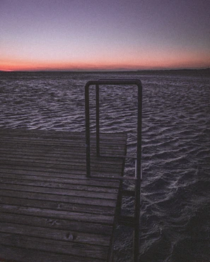 A rustic wooden dock stretching into calm tidal waters under a pastel sky.