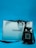 A black Chanel perfume bottle is placed next to a white Chanel shopping bag with black handles. The background is a solid blue color, creating a contrast that highlights the elegance of the items.