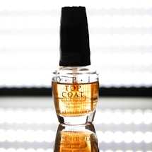 A clear bottle of OPI top coat nail polish stands on a reflective surface. The label on the bottle is visible with black text, and there is a dark-colored cap on top. The background is bright and evenly lit, enhancing the visibility of the product.