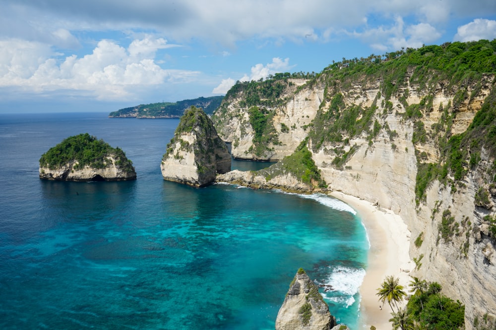 brown and green rock formation on blue sea under blue and white cloudy sky during daytime