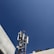 A telecommunications tower equipped with various antennas and equipment surrounded by buildings. The sky is clear and blue, providing a stark, expansive background.