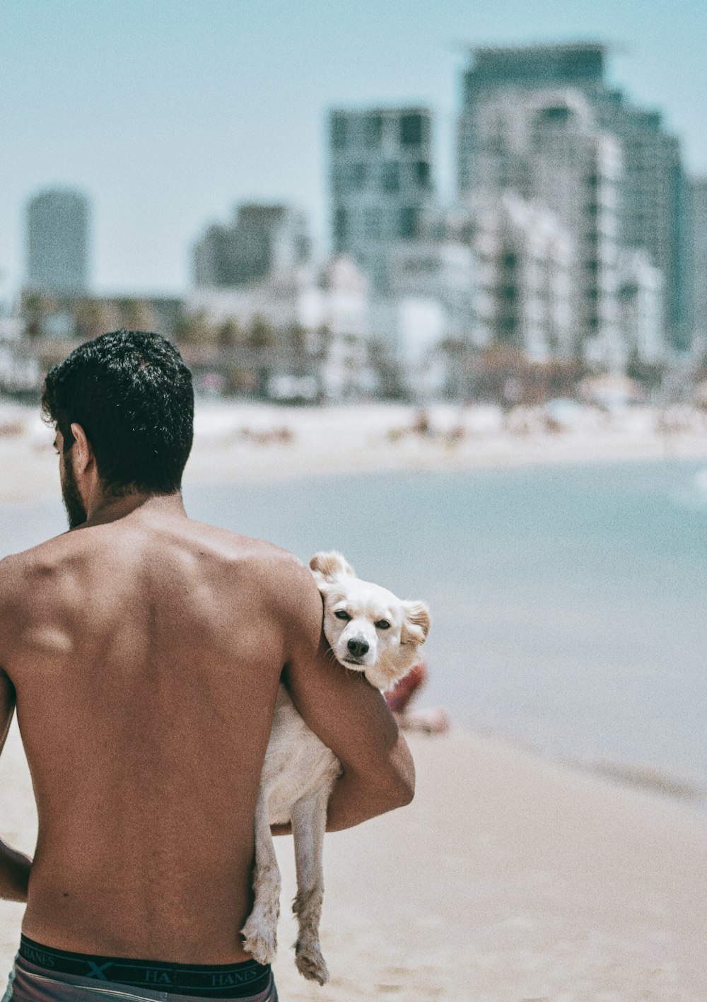 Hombre en topless que lleva un cachorro blanco en la playa durante el día