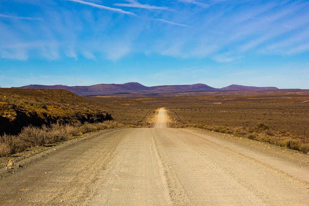 Camino de tierra marrón entre el campo de hierba verde bajo el cielo azul durante el día