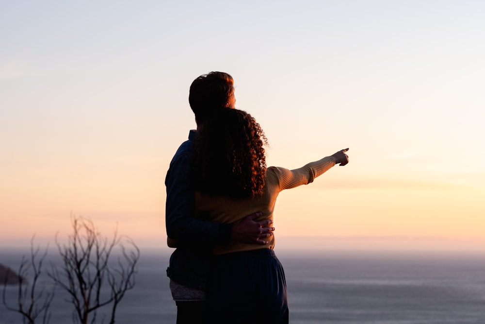 man in black jacket standing and holding camera during sunset