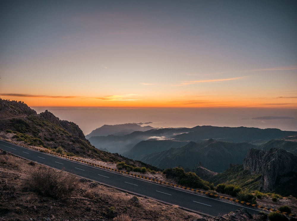 Schwarze Asphaltstraße in der Nähe von Bergen bei Sonnenuntergang