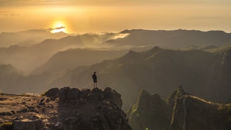 silhouette of person standing on rock formation during daytime