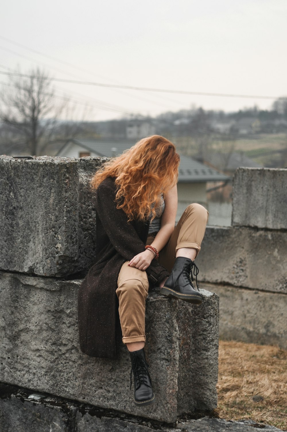 Femme en chemise à manches longues marron et pantalon marron assise sur un mur de béton gris pendant la journée