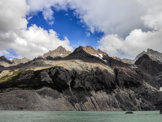 brown and green mountain beside body of water under blue sky and white clouds during daytime in Torres del Paine National Park, Los Perros Glacier Chile