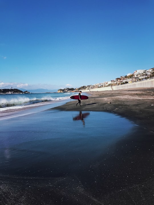 person in red jacket standing on beach during daytime in Kamakura Japan