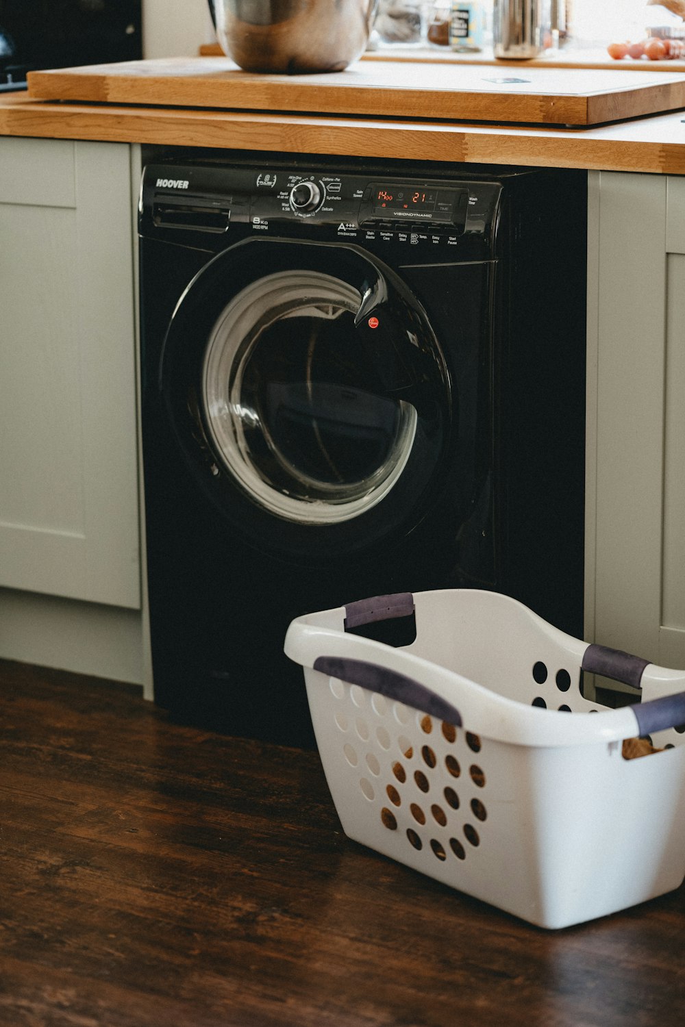 panier à linge en plastique blanc à côté de la machine à laver à chargement frontal noir