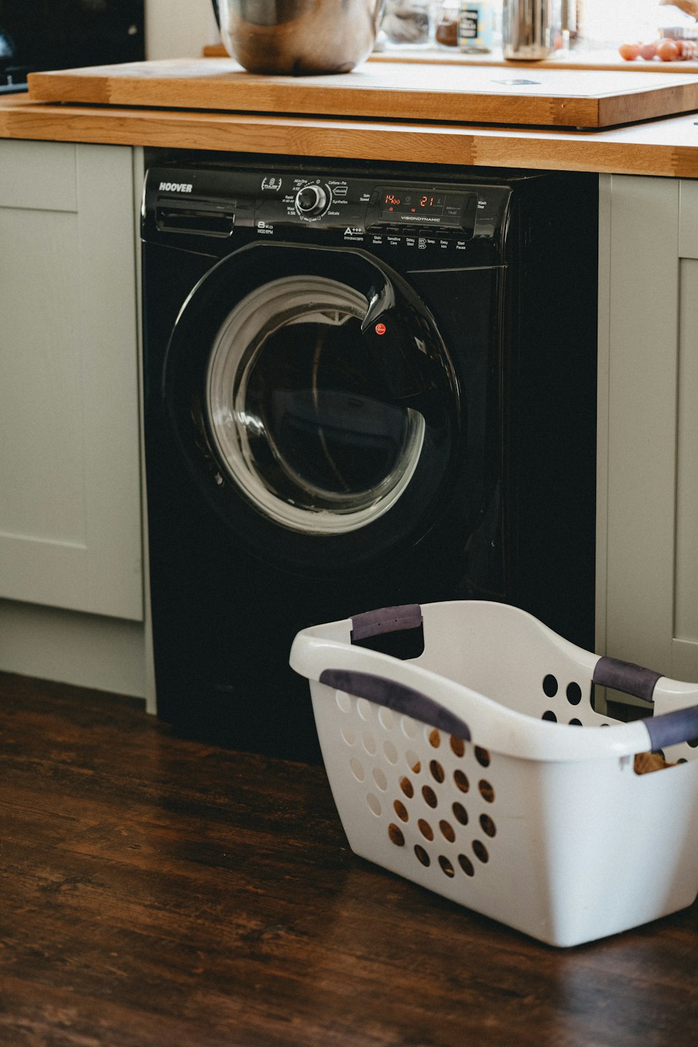 weißer Kunststoffwäschekorb neben schwarzer Frontlader-Waschmaschine