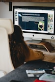 woman in black shirt sitting in front of silver imac