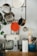 A kitchen scene featuring various utensils and appliances. Several pots and pans hang from a rack, accompanied by a red silicone trivet and kitchen graters. Below, a kitchen mixer with a glass bowl sits next to a roll of paper towels. Nearby, a container holds kitchen tools, including a rolling pin and whisk.