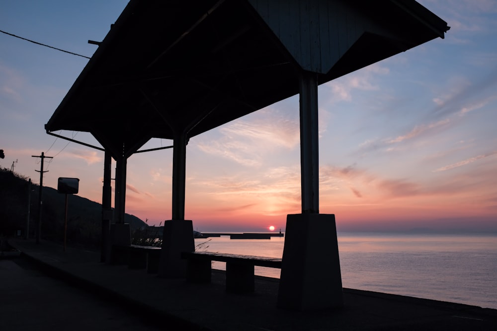 silhouette of bench near body of water during sunset