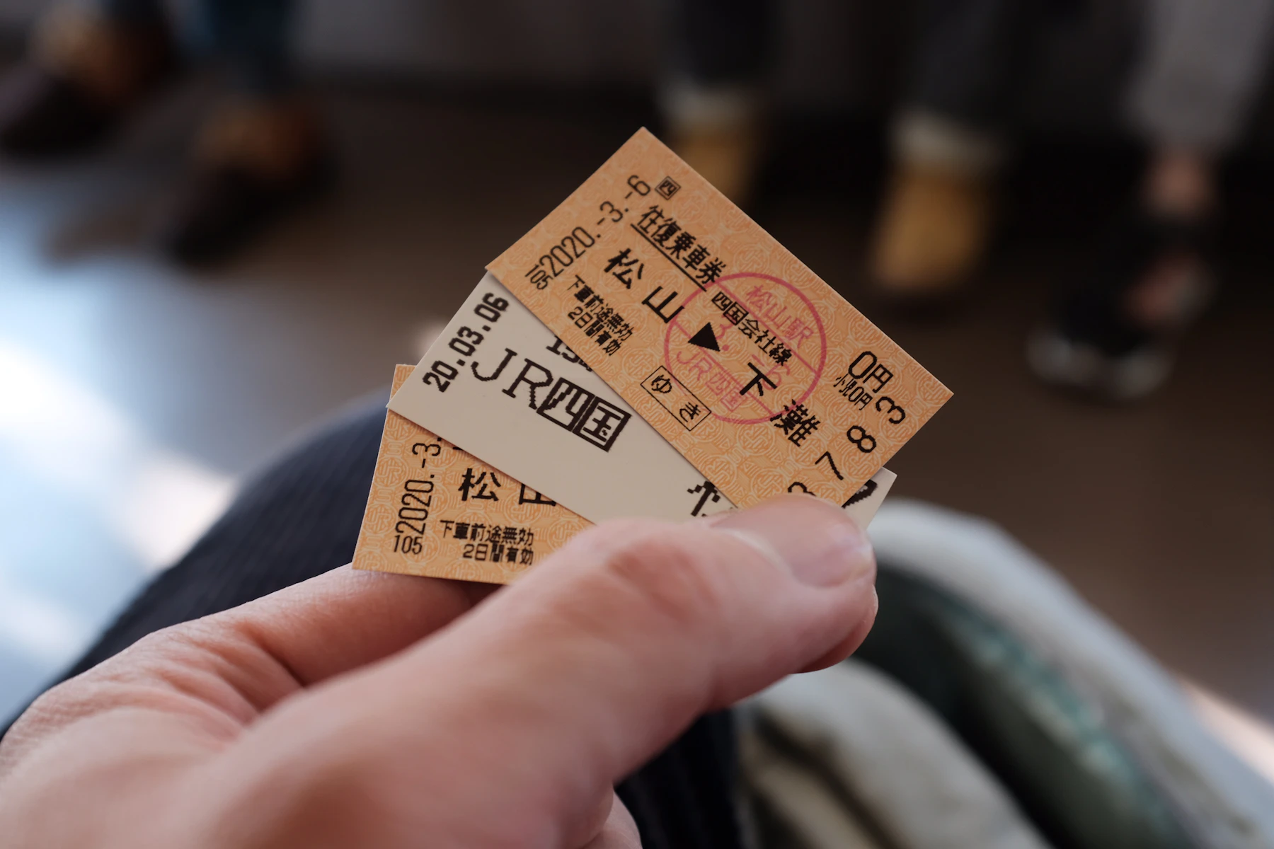 A hand holding three small printed Japanese railway tickets, one with a red date stamp