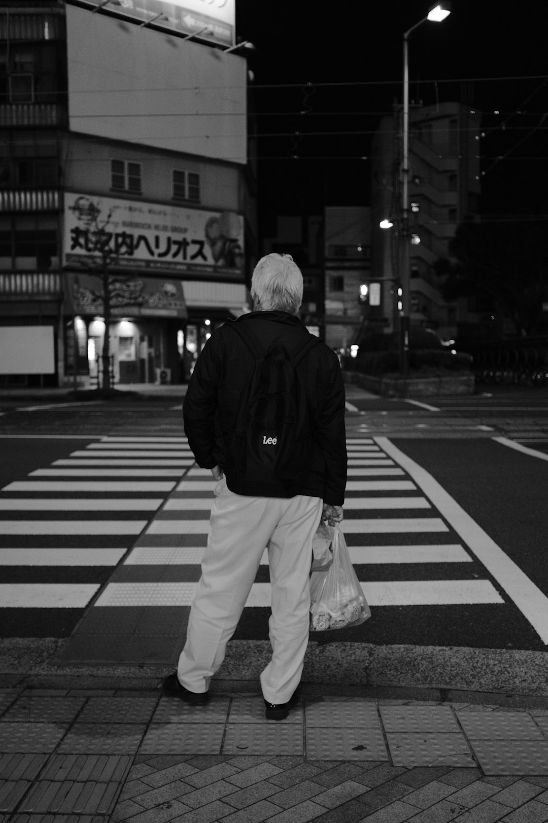 man in black jacket and white pants walking on pedestrian lane in grayscale photography