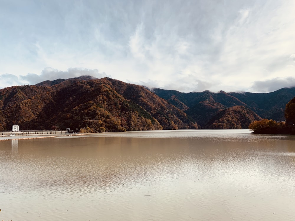 brown mountains beside body of water under white clouds during daytime