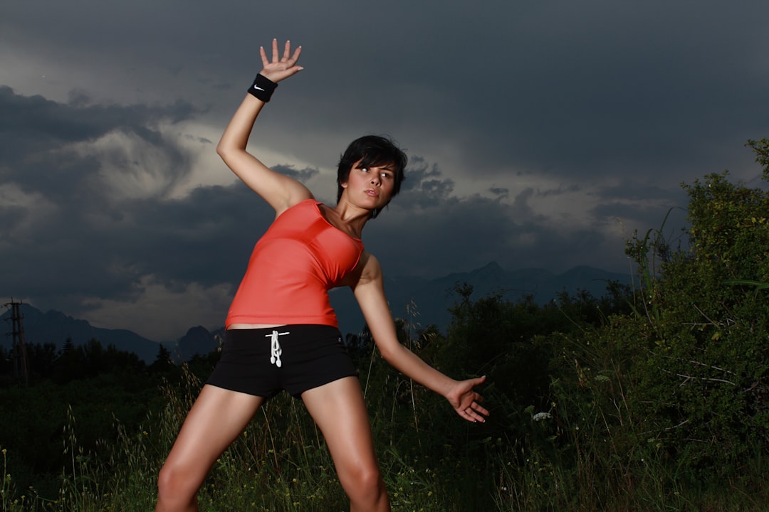 woman in orange tank top and black shorts standing on green grass field under gray cloudy