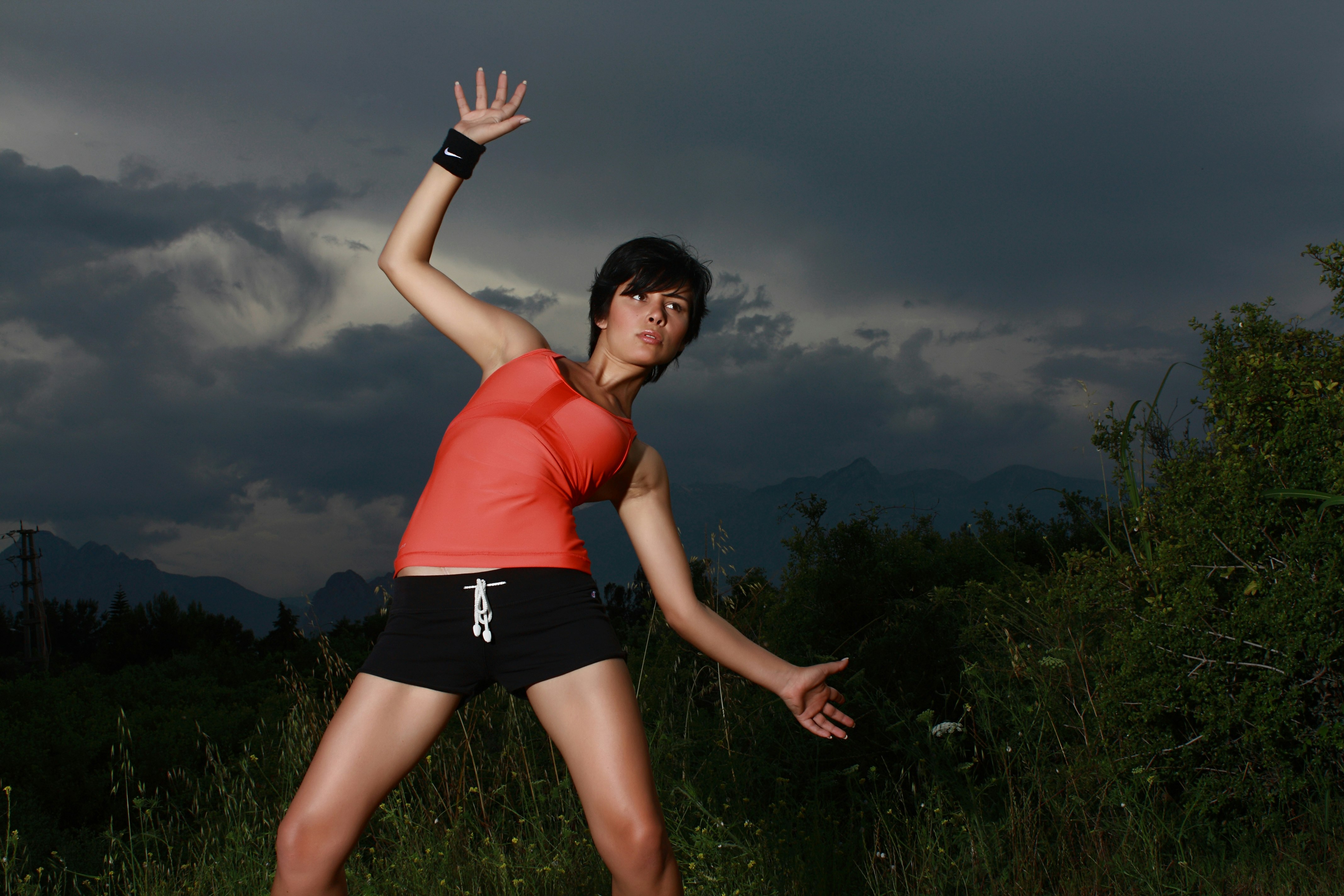 woman in orange tank top and black shorts standing on green grass field under gray cloudy