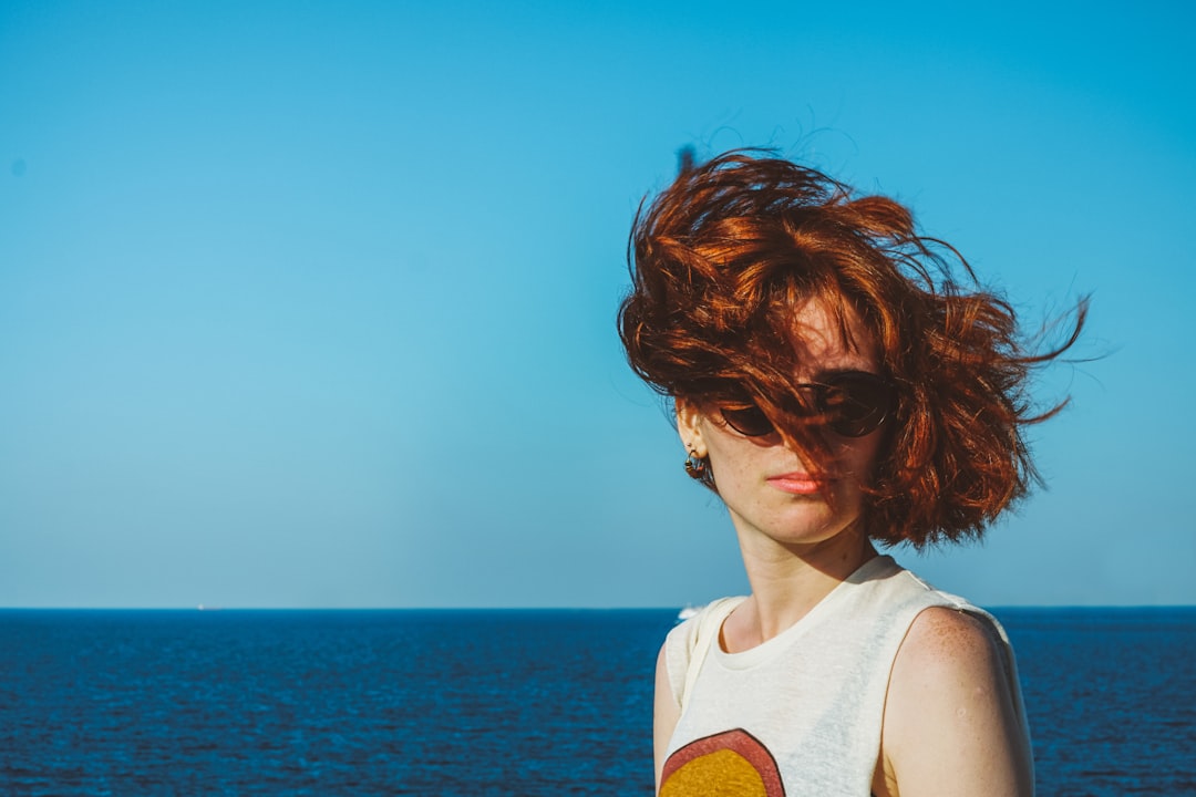 woman in white tank top wearing sunglasses looking at the sea during daytime