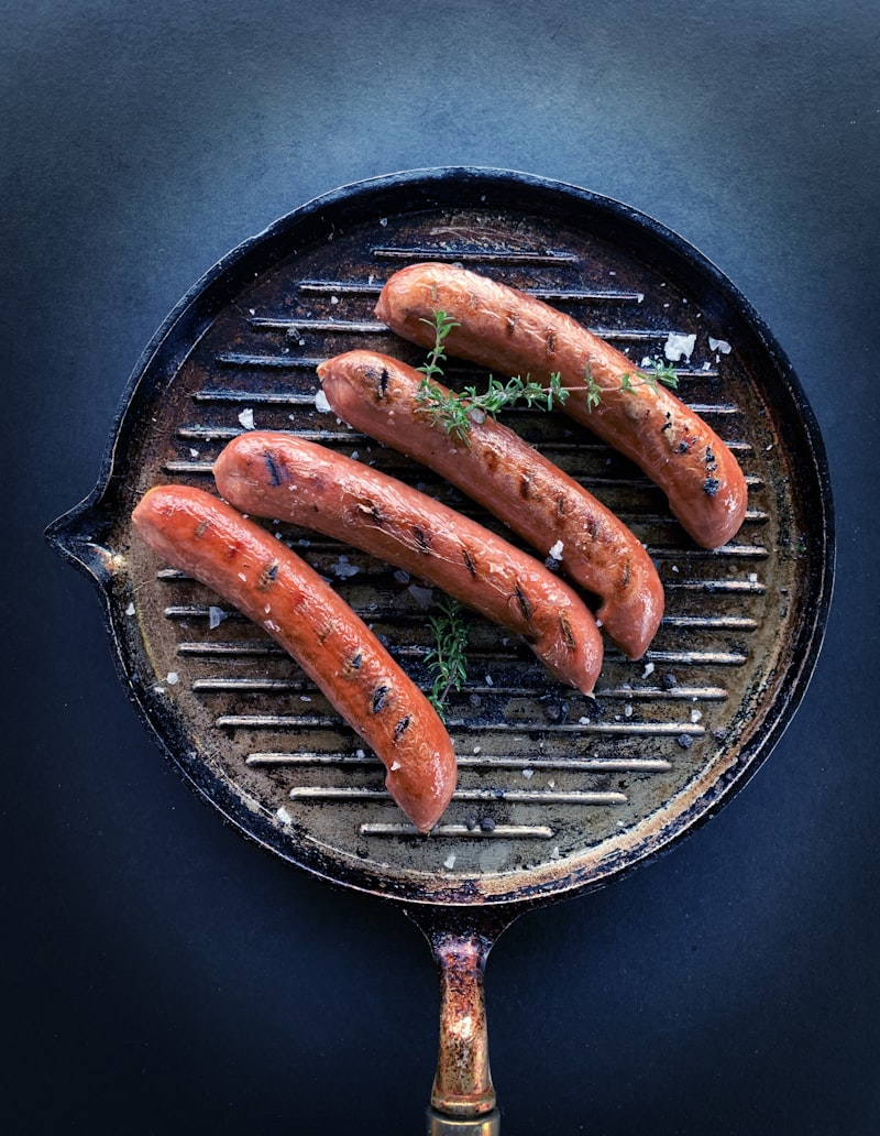 Grilled smoked sausages resting on a dark cast iron grill pan with a sprig of thyme