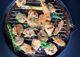 fried meat with green vegetable on black pan