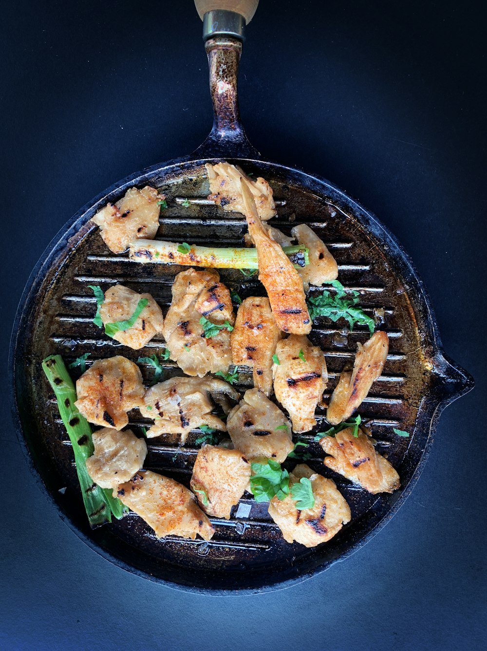 fried meat with green vegetable on black pan