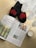 A pair of black slippers with red heart patterns is placed on a wooden floor next to a magazine and a semi-transparent lace curtain. The magazine has an article with text and images of food, possibly a healthy lifestyle or recipe section. Beside the magazine is a glass mug filled with a frothy beverage.