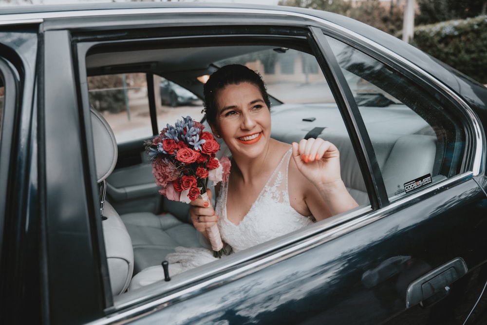woman in white wedding dress holding bouquet of flowers inside car