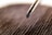 A close-up view of a screwdriver tip positioned above a textured surface, possibly a piece of fabric or wood. The focus is on the screwdriver, with the background appearing slightly blurred.