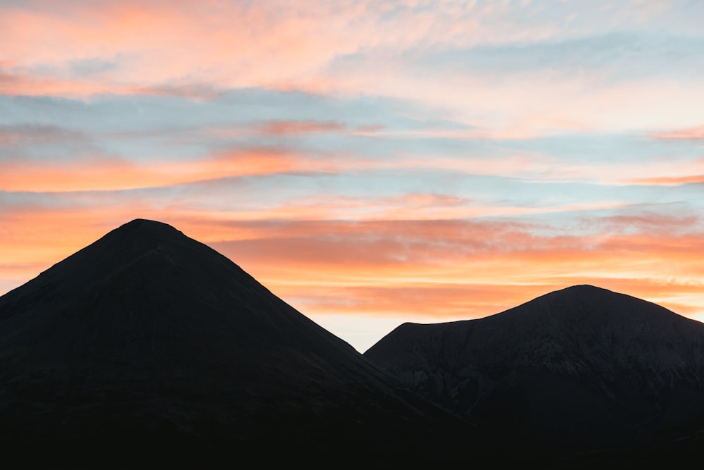 silhouette of mountain under cloudy sky during sunset