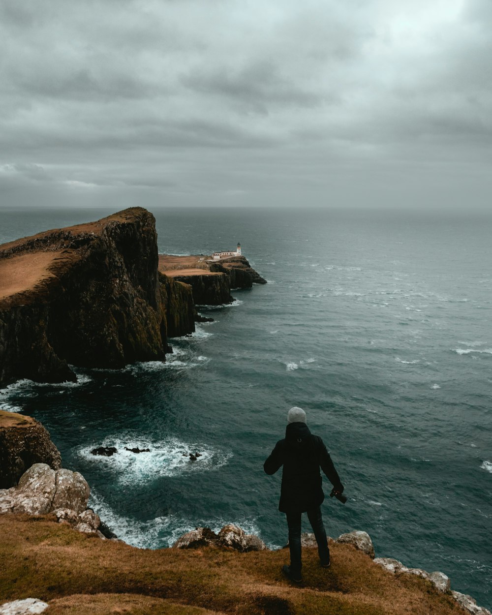 man in black jacket standing on brown rock formation near body of water during daytime