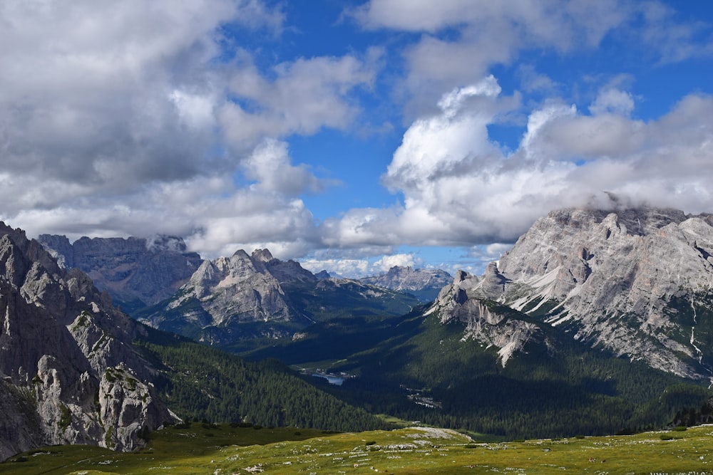 green grass field and mountains under white clouds and blue sky during daytime