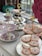 An elegant tea setting features tiered trays adorned with ornate cookies, some of which display a recognizable logo. A decorative cup and plates with floral designs add to the sophisticated aesthetic. A lush bouquet of pink roses complements the setting, adding a touch of vibrant color.