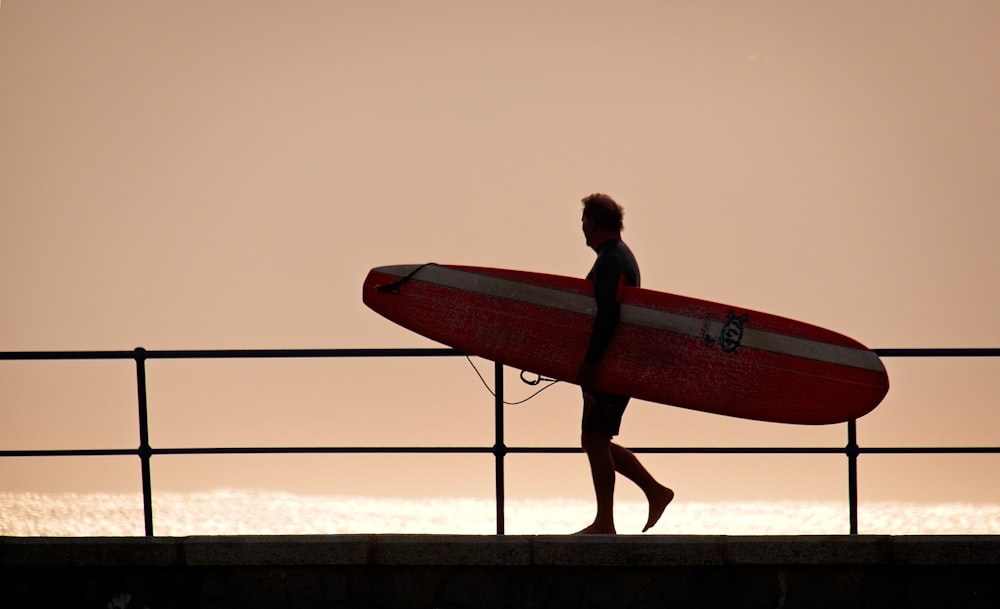 man in black wet suit carrying red surfboard