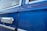 Close-up of a classic car door with a shiny chrome handle against a vibrant blue paint finish. The window features a slight reflection and is bordered by chrome trim, adding to the vintage appeal.