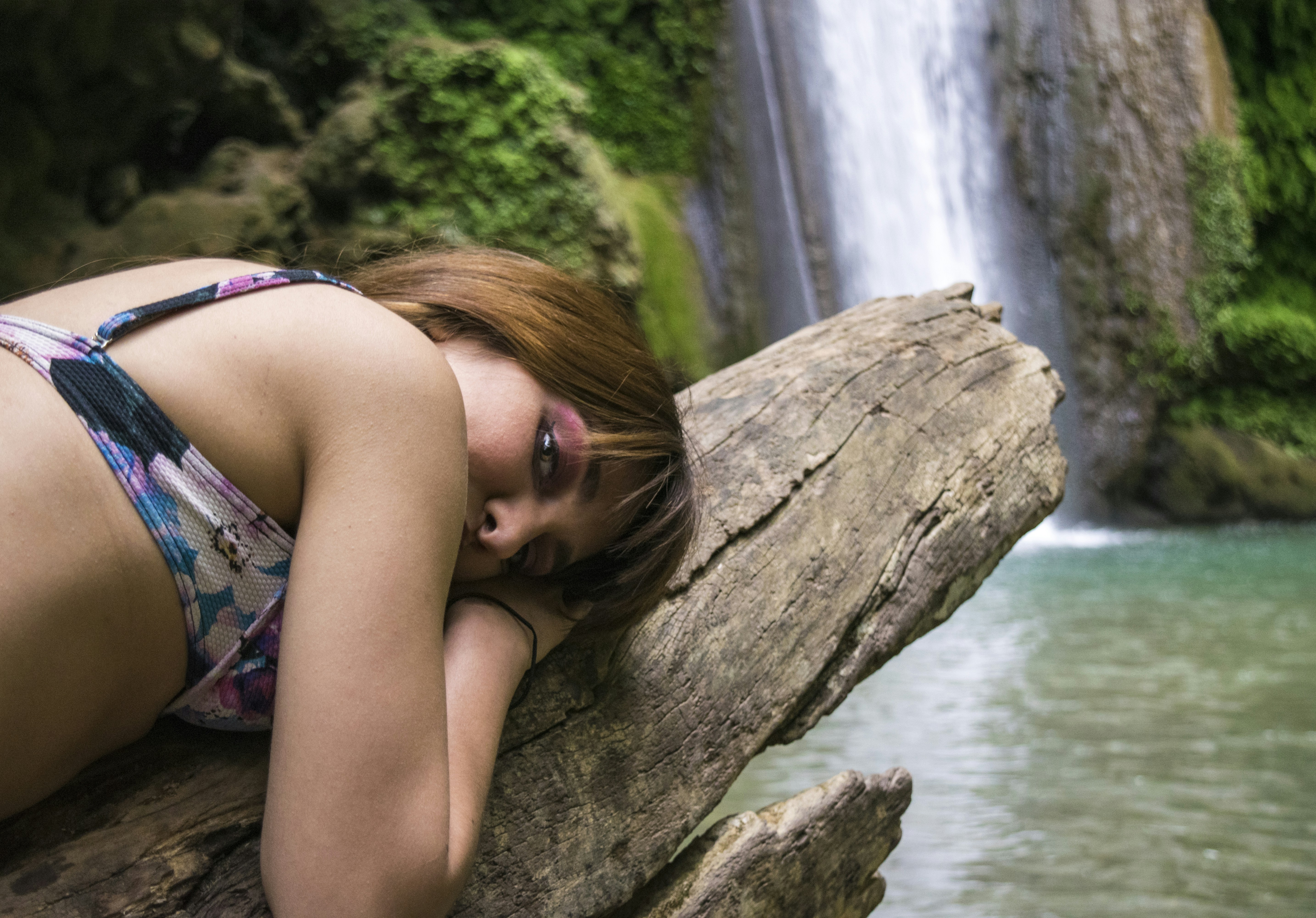 woman in purple and black floral tank top wearing black sunglasses sitting on brown tree trunk
