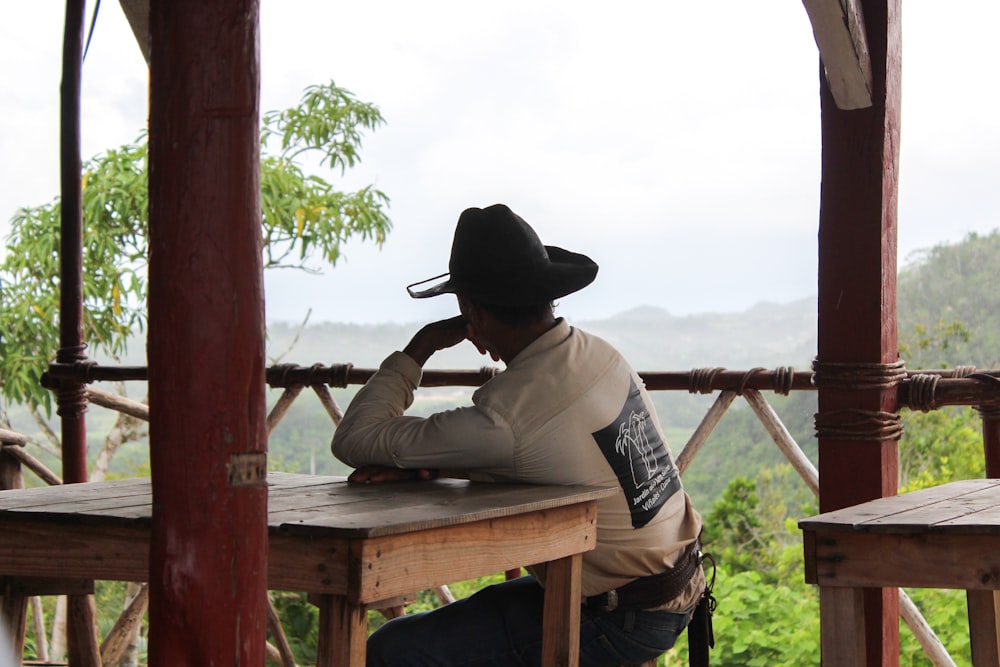 Homme en chemise blanche et chapeau de cow-boy marron assis sur un banc en bois marron