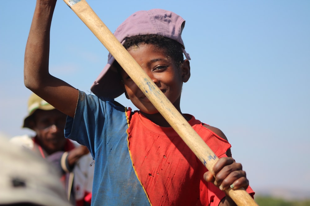 man in blue and red shirt holding brown wooden stick