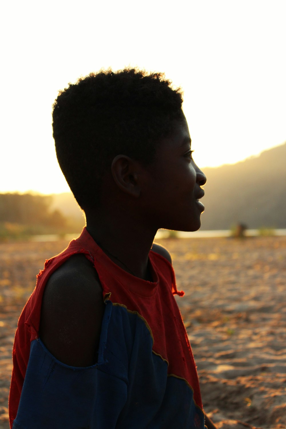 boy in orange and blue tank top standing on brown sand during daytime