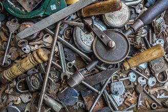 A collection of various mechanical tools and keys arranged in a chaotic manner. The image includes a variety of metallic objects such as locks, wrenches, keys, and a hand drill, among others. The items display signs of wear and use, giving a vintage and rustic feel.