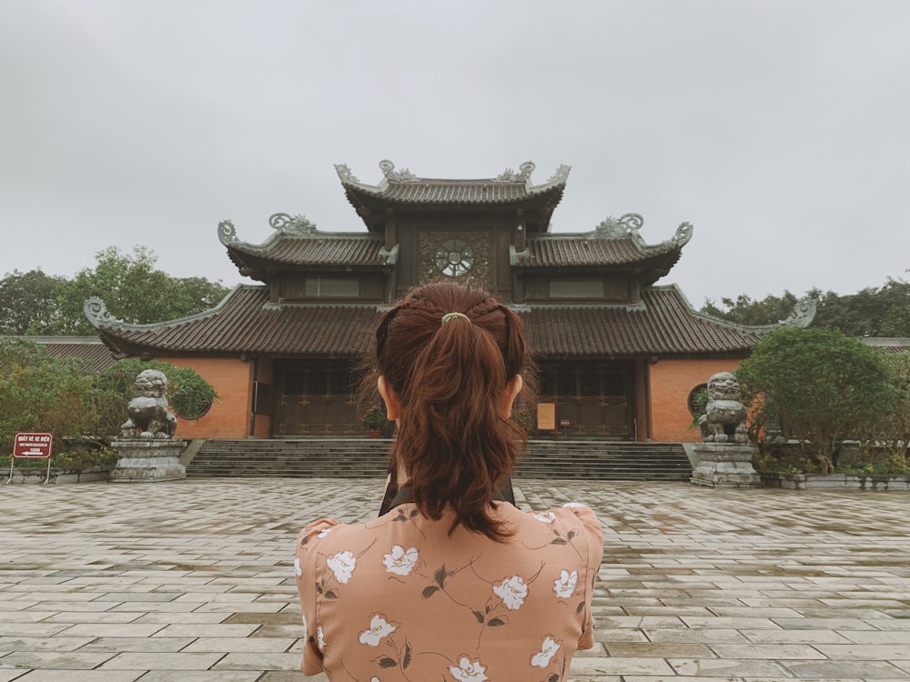 woman in white and red floral shirt standing near temple during daytime