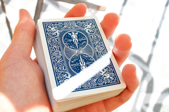 Elegant hands holding tarot cards with soft golden light and a deep blue marbled background.