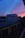 A residential neighborhood at dusk featuring a prominent building against a dramatic sky. The sunset casts vibrant shades of blue, pink, and orange across the horizon. The scene includes rows of garage rooftops, with some dimly lit windows visible in the building.