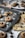Freshly baked cookies topped with chocolate kisses are placed on a dark baking tray, dusted with powdered sugar. Surrounding the tray are additional cookies and chocolate kisses on light-colored plates and cloths, some scattered crumbs, and a white cup in the background.