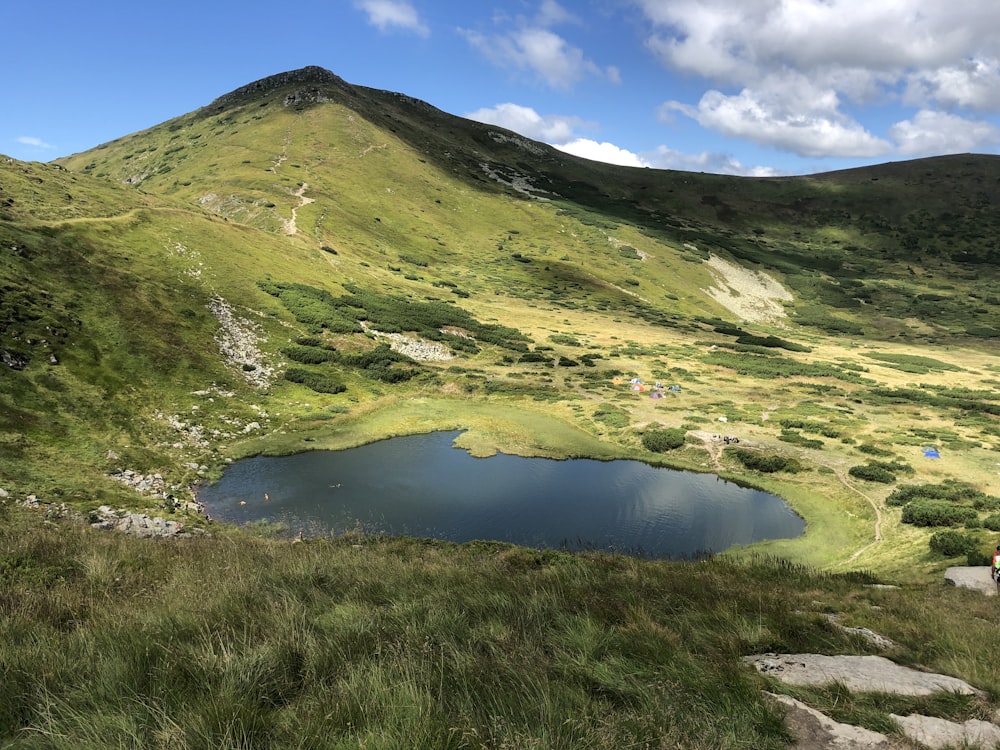 green mountain beside lake under blue sky during daytime