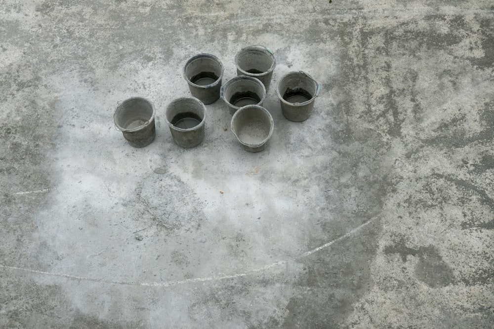 灰色のコンクリートの床に8つの灰色の金属の丸い容器